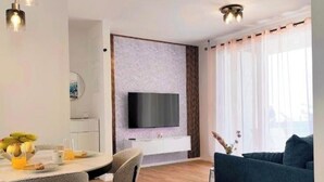 Ein modernes Wohnzimmer mit Fernseher, einer Couch, einem Esstisch, Stühlen und Holzboden.