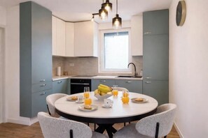 A modern kitchen with teal cabinets, a round dining table, and a window providing natural light.