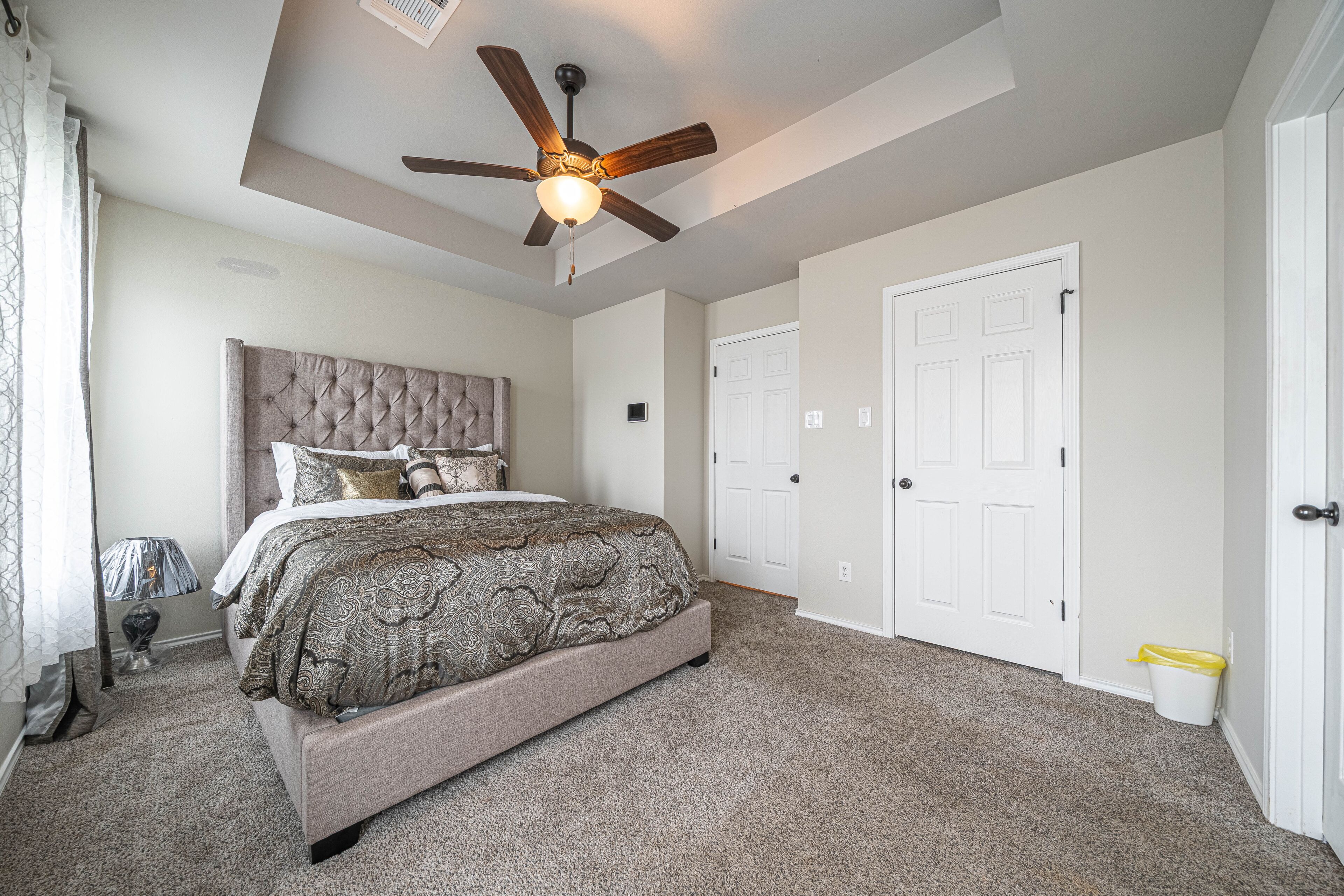 A bedroom with a bed, ceiling fan, carpeted floor, and white doors.