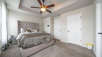 A bedroom with a bed, ceiling fan, carpeted floor, and white doors.