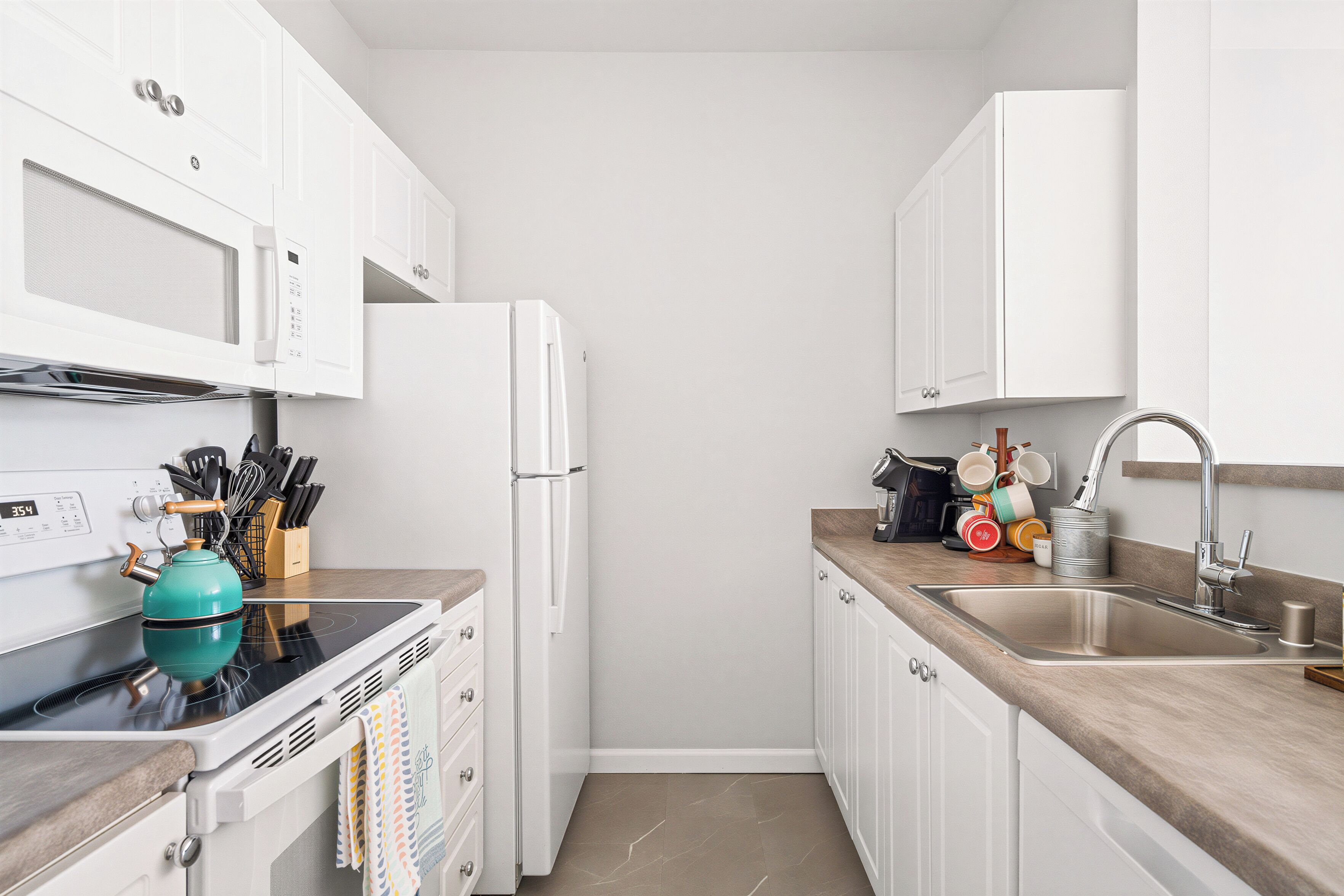 A modern kitchen with white cabinets, a stainless steel sink, a microwave, and a teal electric kettle.