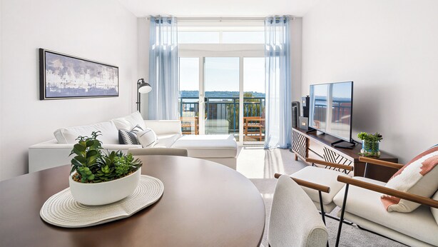A modern living room with a sofa, a dining table with a plant, a TV, and a balcony with a view. - Elliott Bay View Condo Near Everything and Seattle Center with AC and More! (Seattle)