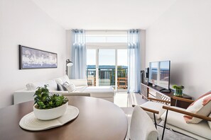 Una sala de estar moderna con un sofá, una mesa de comedor con una planta, un televisor y un balcón con vistas.