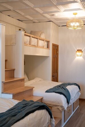 Quarto com beliche, escada, mesa de cabeceira e luminária na parede.