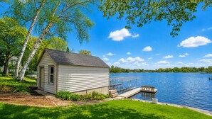 Un piccolo chalet sul lago con un molo, circondato da vegetazione e alberi.