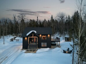 Eine zweistöckige Holzhütte mit Veranda, einer Terrasse und einem Kamin.