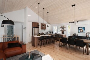 A modern kitchen with a central island, bar stools, and a dining area with a wooden table and chairs. - Mystérieux, Pool, Spa & Sauna,  Billard & Games (Matawinie Regional County Municipality)