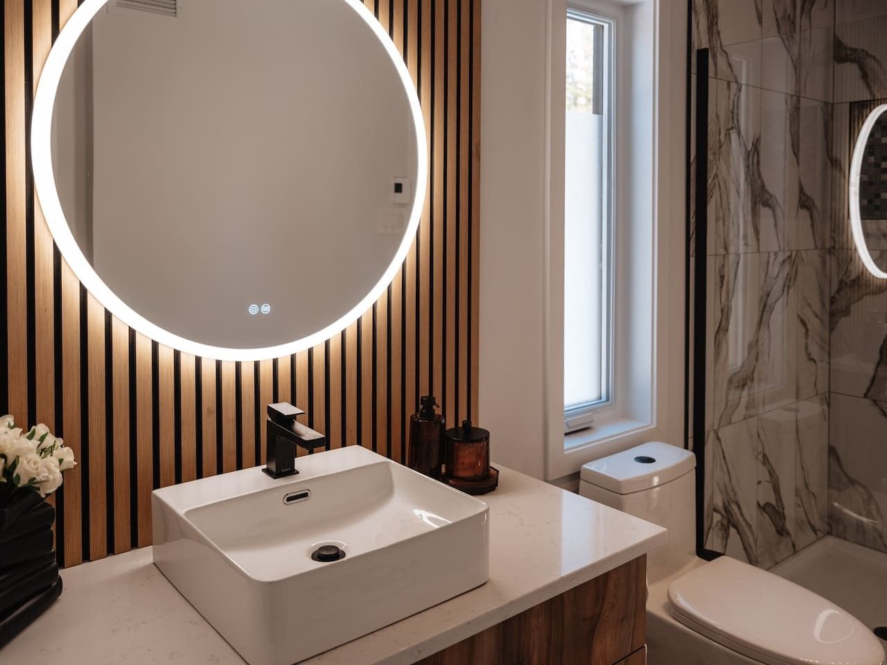 Un baño moderno con un espejo grande, un lavamanos blanco y un inodoro.