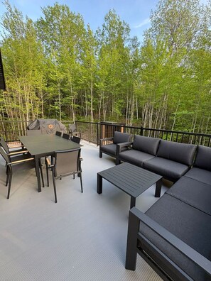 Ein Außenbereich mit Terrasse, Tisch, Stühlen, einer Sitzecke und einem überdachten Grill.