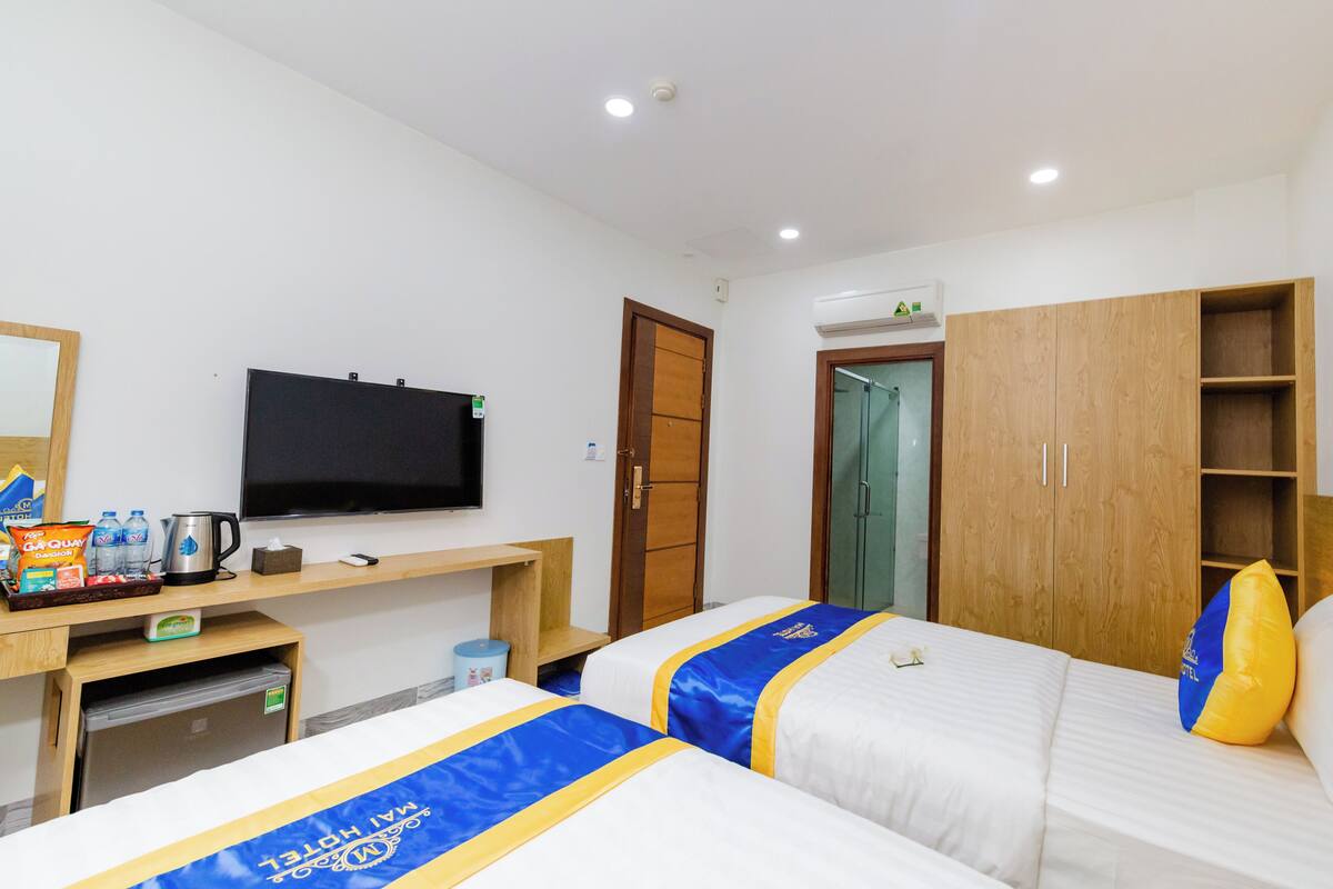 Ein Hotelzimmer mit zwei Betten, einem Fernseher, einer Minibar und einem Holzschrank.