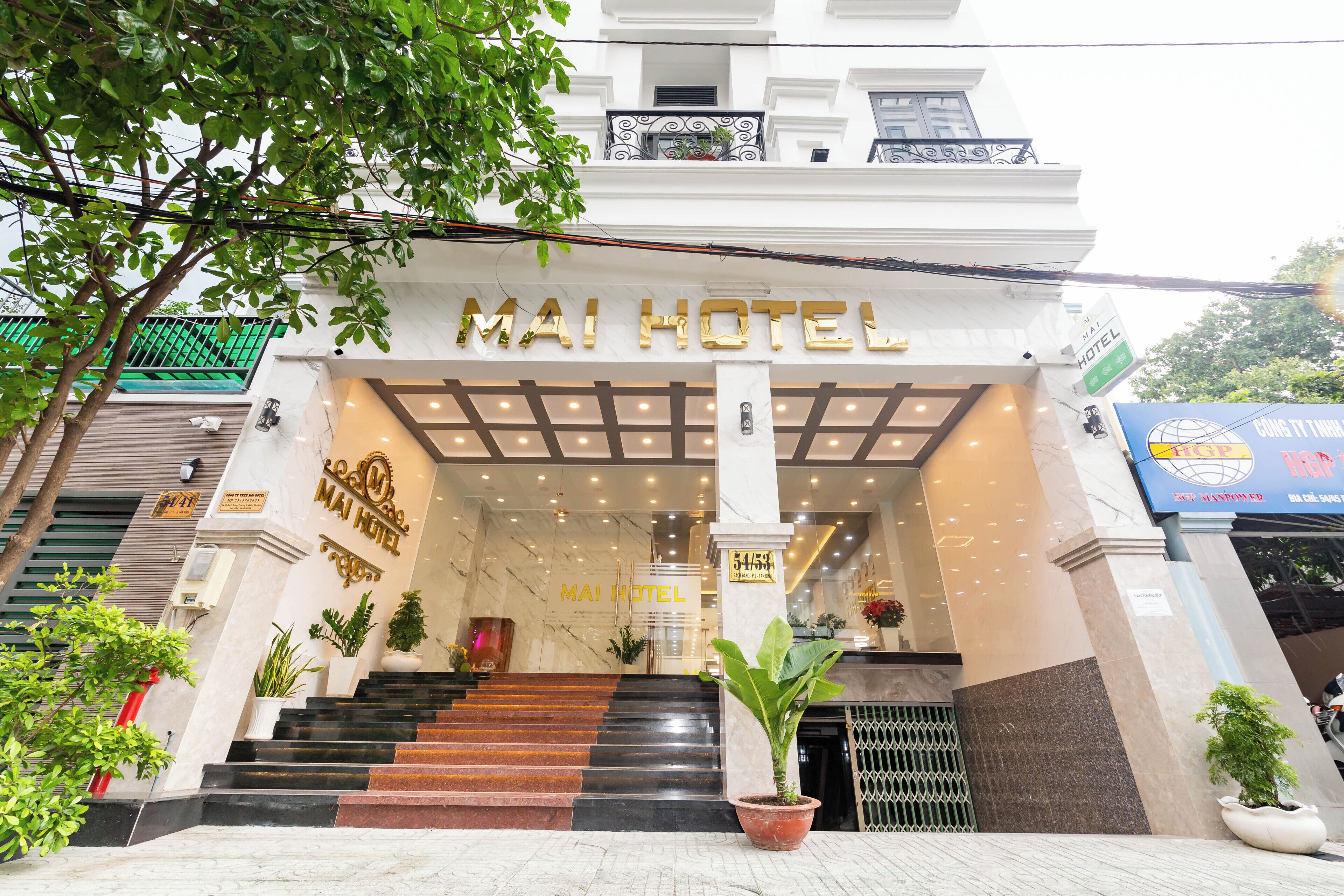La entrada del Hotel Mai, con fachada de mármol, una escalera que conduce a la entrada y plantas en macetas.
