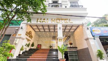 La entrada del Hotel Mai, con fachada de mármol, una escalera que conduce a la entrada y plantas en macetas.