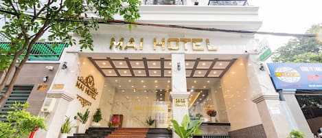 Entrada do Hotel Mai com fachada de mármore, escadaria que leva à entrada e plantas em vasos.