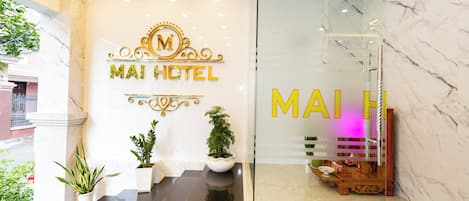 A hotel entrance with a marble floor, potted plants, and a glass door leading inside.