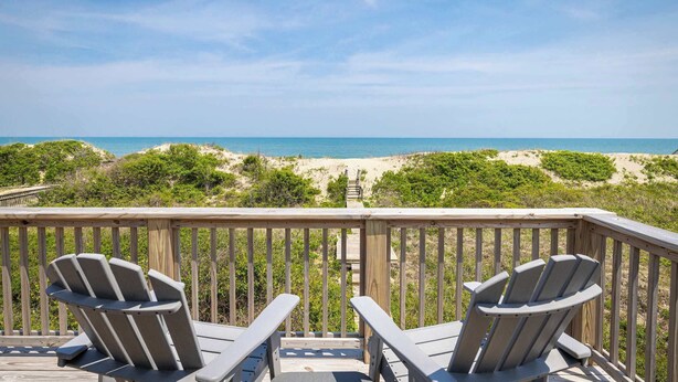 Una terraza de madera con dos sillas Adirondack con vista a la playa.