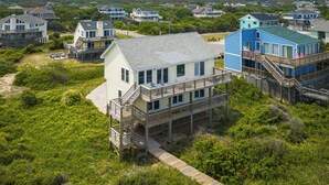 Una casa frente al mar con una terraza de madera, un balcón y una escalera que lleva al segundo piso.