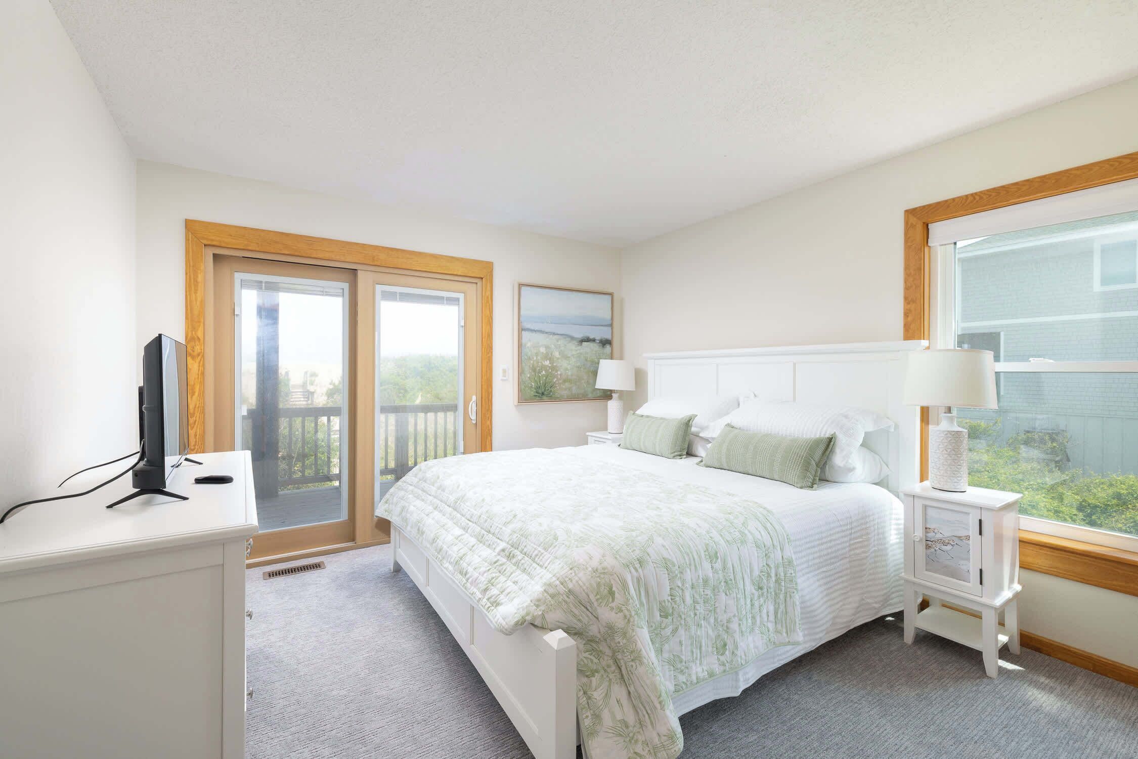 A bedroom with a bed, a nightstand, a lamp, a TV, and a window with a view.