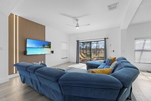 A modern living room with a flat-screen TV, a blue sofa, and a sliding glass door leading to an outdoor area. - New! Perfect Summer Retreat. Pool/Spa. 2 Kings (Clermont)