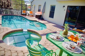 A swimming pool with a curved edge, green chairs, and a table set with plates, cups, and a pineapple. - New! Perfect Summer Retreat. Pool/Spa. 2 Kings (Clermont)