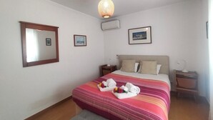 Quarto de hotel com cama, mesa de cabeceira, ar-condicionado fixado na parede e luminária no teto.