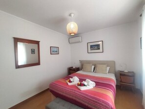A hotel room with a bed, a nightstand, a bedside table, a wall-mounted air conditioner, and a ceiling light fixture. - Apartment in Front of the Sea (Gafanha da Encarnação)