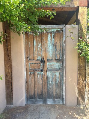 Une porte en bois rustique, dotée d’un loquet en métal, est encastrée dans un mur usé dont la peinture s’écaille.