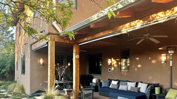 A covered patio area with outdoor seating, a table, and a decorative tree stump. - Raven's Haven in the Heart of Santa Fe (Santa Fe)