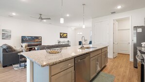 Eine moderne Küche mit Granit Arbeitsplatten, Edelstahlgeräten und einem Essbereich mit grauem Sofa und Flachbildfernseher.