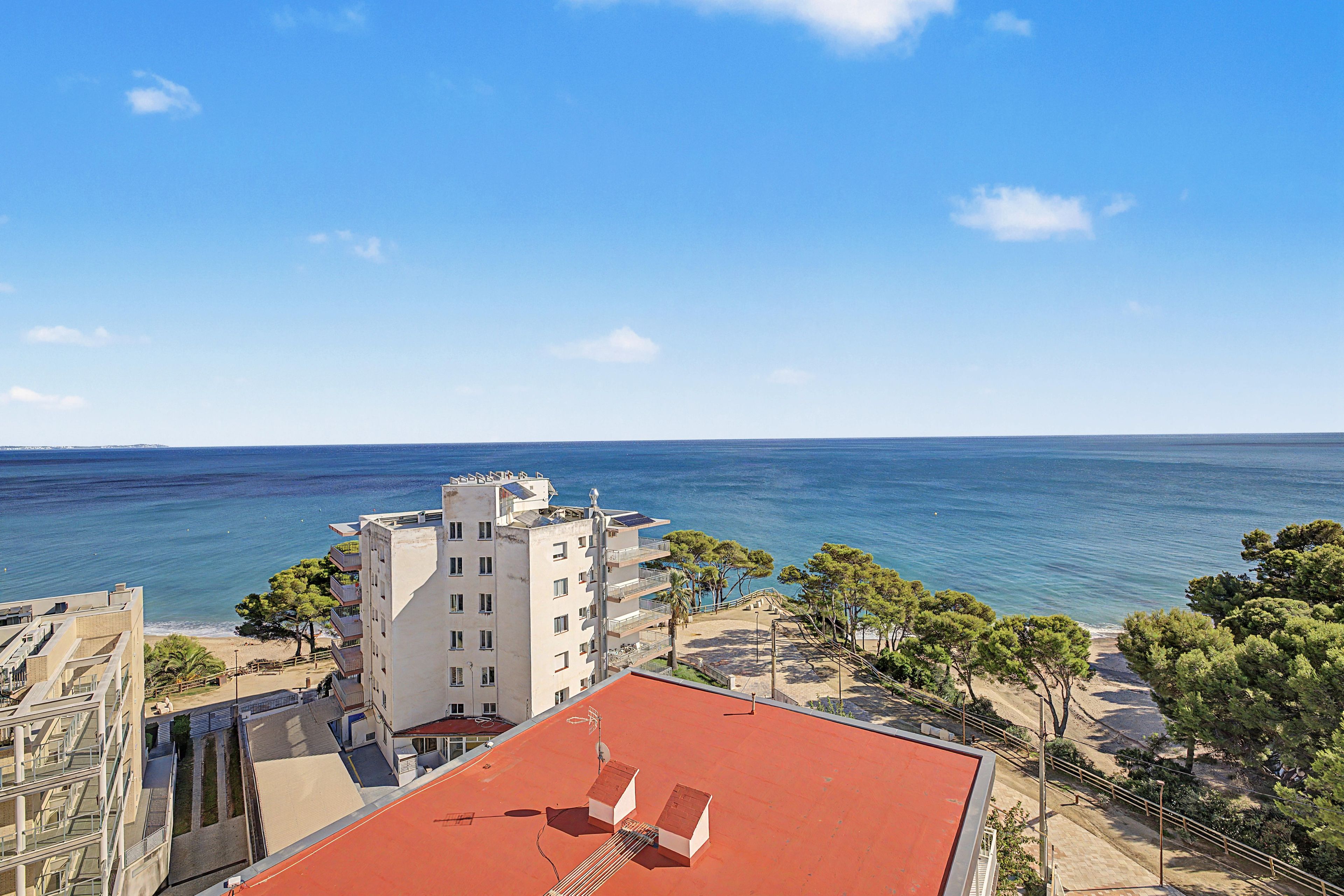 A coastal building with a red roof, overlooking a beach and the sea.