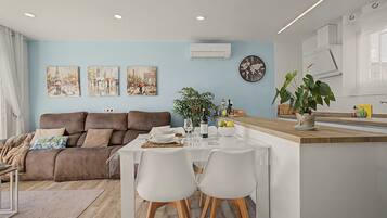 Un salon moderne avec un canapé marron, une table à manger dressée pour deux personnes et un coin cuisine doté d’un plan de travail en bois.