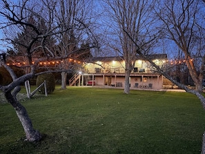 Una casa de dos pisos con un porche cubierto, mobiliario exterior y luces colgantes.