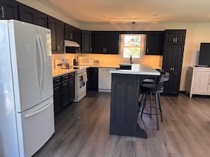 Una cocina moderna con armarios oscuros, un refrigerador blanco, microondas, estufa y una zona de bar con taburetes.