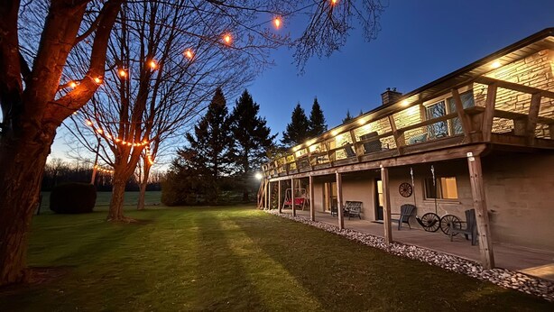 A two-story building with a covered patio area, outdoor seating, and string lights. - Ingrid’s Green Haven - 27 Acre Private Farm (Wiarton)