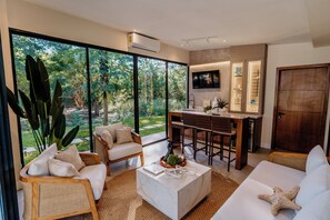 A modern living room with a large window, a kitchen area, and a seating area. - Luxury Villa In Los Cobanos Sonsonate (Acajutla)
