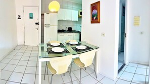 A dining area with a glass table, four chairs, and a white refrigerator. - Vacanze - Neo (Maceió)