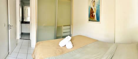 Une chambre d’hôtel avec un lit, un tableau accroché au mur, une salle de bain visible à travers une porte ouverte et un sol carrelé.