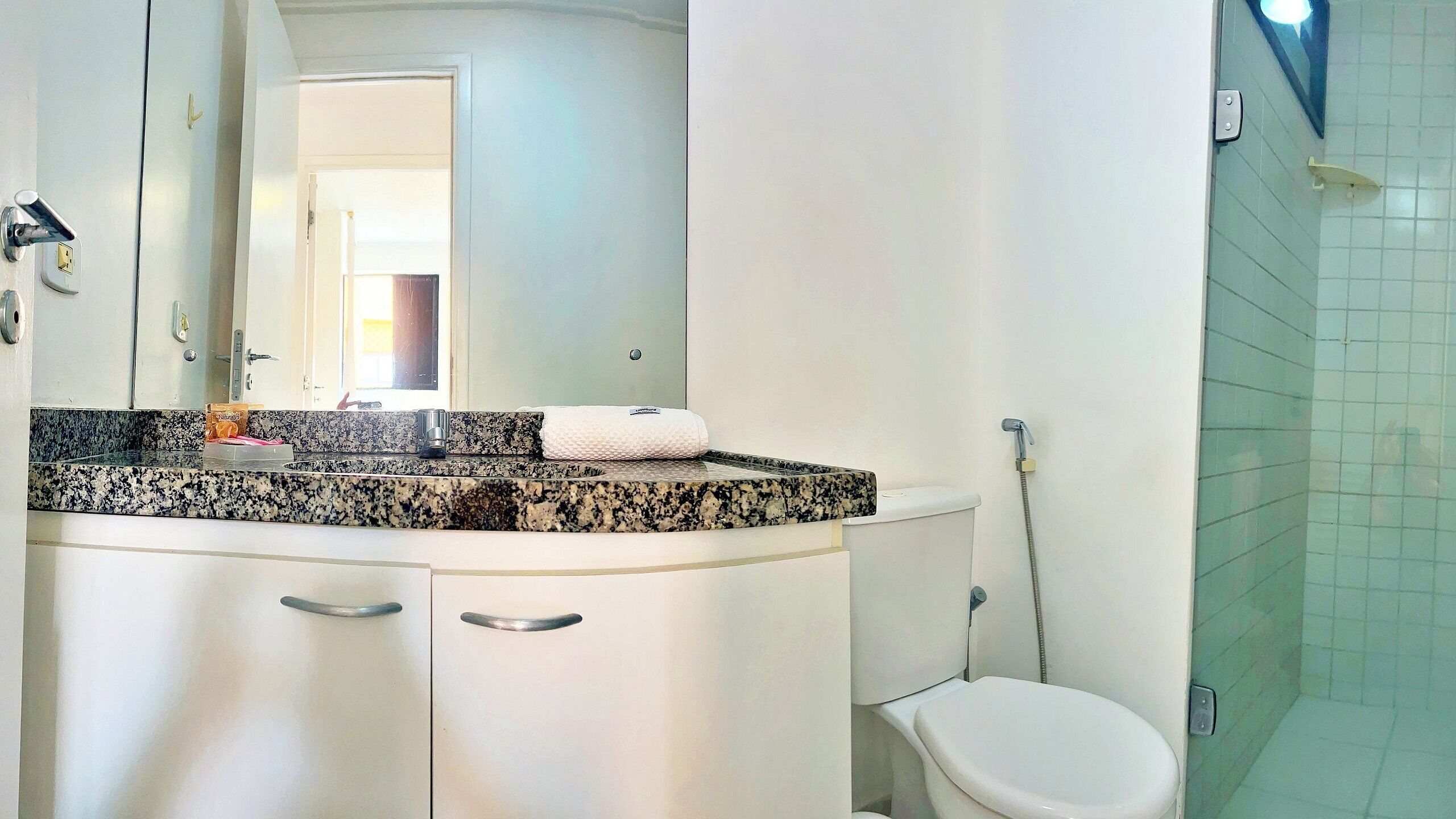 A bathroom with a white toilet, a granite countertop, a mirror, and a shower.
