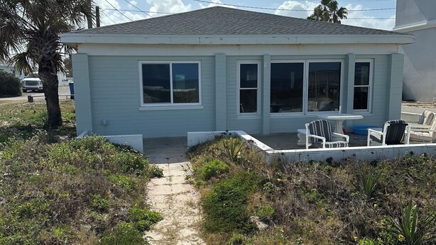 Une maison de plain-pied avec une allée pavée menant à un porche d’entrée agrémenté de mobilier d’extérieur.