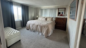 Une chambre à coucher avec un lit, une commode, un miroir et une fenêtre avec des rideaux.