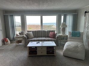 A living room with a sofa, armchair, coffee table, and a view of the beach. - Private Beachfront 2BR Getaway, Sleeps 6, Steps to the Sand, Ormond-by-the-Sea (Ormond Beach)