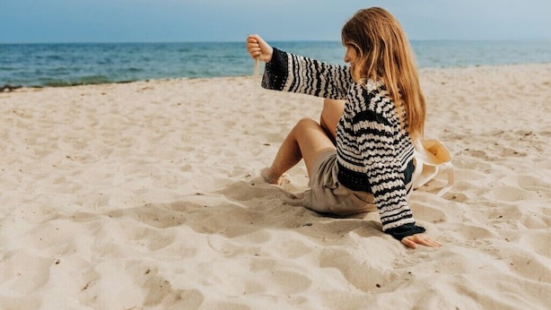 A person sitting on a sandy beach with the ocean in the background.