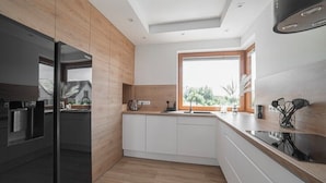 A modern kitchen with a black refrigerator, wooden cabinets, a window with a view, and a countertop with a sink.