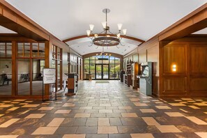 Um hall amplo com piso xadrez, vigas de madeira, um lustre e grandes janelas com vista.