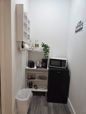 Una cocina compacta equipada con microondas, cafetera y un cubo de basura.
