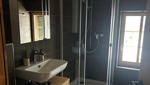 A modern bathroom with a glass-enclosed shower, a sink with a mirror above, and a wooden cabinet. - Delightful 3-bedroom apartment in charming Frutigen awaits you (Frutigen)