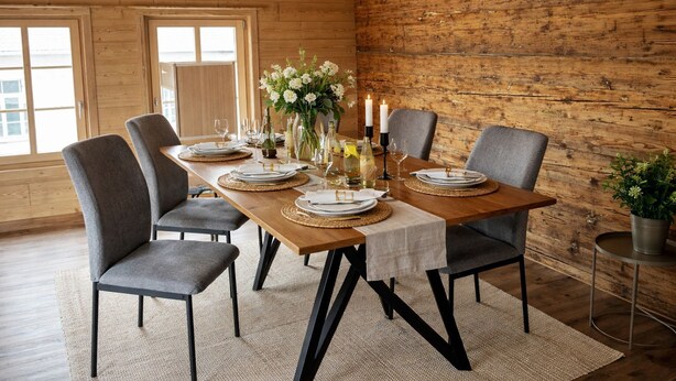 A dining room with a wooden table set for six, surrounded by grey chairs, with a rustic wooden wall and large windows. - Delightful 3-bedroom apartment in charming Frutigen awaits you (Frutigen)