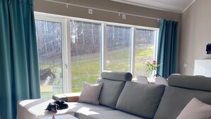 Ein modernes Wohnzimmer mit grauem Sofa, einem weißen Couchtisch und einem großen Fenster mit Vorhängen.