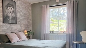 Ein Schlafzimmer mit einem Bett, einem Fenster mit Vorhängen, einer Wandleuchte und einem gerahmten Bild.