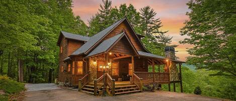A log cabin with a porch, stone chimney, and a driveway leading to the entrance.