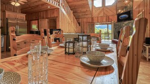 Interior de uma cabana de madeira, com uma mesa de jantar posta para quatro pessoas, um frigorífico e uma televisão fixada numa parede de pedra.